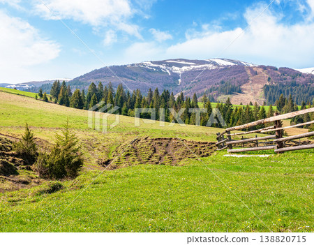 mountainous countryside landscape in spring. wooden fence and grassy meadow on a green hill. distant mountain ridge with snow capped tops. sunny weather with blue sky. natural carpathian image mountainous countryside landscape in spring. wooden fence and grassy meadow on a green hill. distant mountain ridge with snow capped tops. sunny weather with blue sky. natural carpathian image 138820715