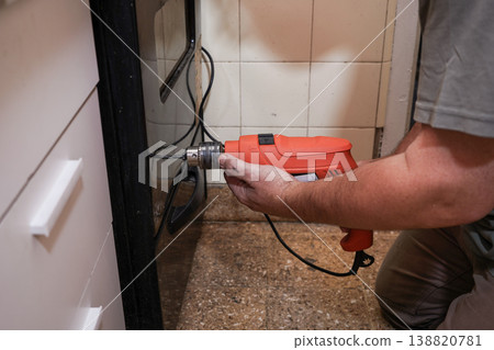 A man drilling a hole in the oven door of a home kitchen 138820781