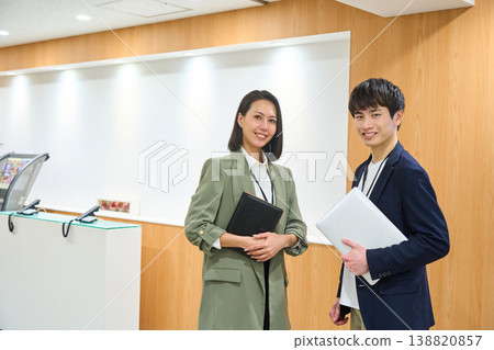 Business professionals, both male and female, line up at a company reception desk, smiling and holding laptops and notebooks. Business professionals, both male and female, line up at a company reception desk, smiling and holding laptops and notebooks. 138820857