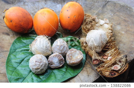 Collection of orange and green betel nuts with broken betel nut shells placed on a textured wooden surface. 138822086