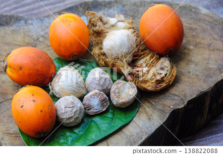 Mixed ripe orange and green betel nuts with split betel nut shells arranged across old wooden planks in a simple rustic flat lay scene. 138822088