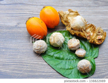 Fresh orange and green betel nuts with opened betel nut shells displayed on an aged wooden background in a natural harvest-style arrangement. Fresh orange and green betel nuts with opened betel nut shells displayed on an aged wooden background in a natural harvest-style arrangement. 138822089