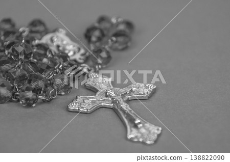 Monochrome Rosary with metallic crucifix and reflective beads displayed on neutral background in a dramatic black and white religious still life. 138822090