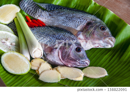 Fresh whole tilapia fish arranged on green banana leaves with lime slices and white mushrooms. 138822091