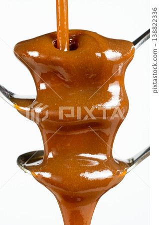 Flowing stream of liquid caramel on white background. Flowing stream of liquid caramel on white background. 138822336