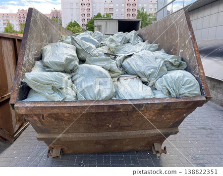 A large dumpster filled with bags of trash in a city area during daylight hours A large dumpster filled with bags of trash in a city area during daylight hours 138822351