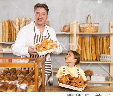 Young daughter helps her father place hot croissants on bakery display. Family business Young daughter helps her father place hot croissants on bakery display. Family business 138822408