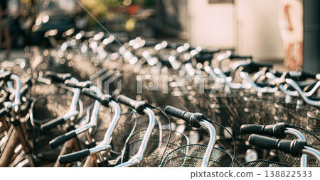 shallow depth-of-field view looking down a long row of handlebars and front baskets of numerous bicycles parked closely together. 138822533