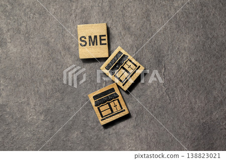SME business concept featuring three wooden blocks with the acronym SME and storefront icons laid flat on a dark textured stone surface, representing small and medium enterprises SME business concept featuring three wooden blocks with the acronym SME and storefront icons laid flat on a dark textured stone surface, representing small and medium enterprises 138823021
