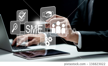 A businessman uses a laptop and digital overlays representing SME growth, partnerships, global reach, and human resources in a professional dark setting A businessman uses a laptop and digital overlays representing SME growth, partnerships, global reach, and human resources in a professional dark setting 138823022
