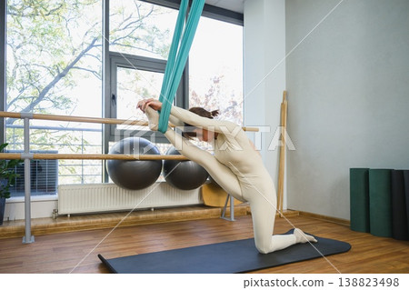 Young woman performing deep stretch with aerial yoga hammock in fitness studio. Young woman performing deep stretch with aerial yoga hammock in fitness studio. 138823498