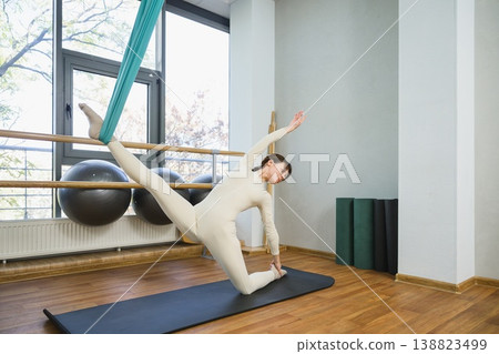 Young woman performing aerial yoga balance with extended leg in fitness studio. Young woman performing aerial yoga balance with extended leg in fitness studio. 138823499