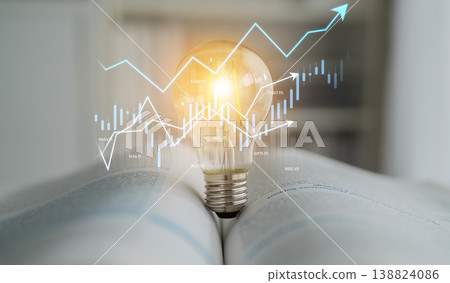 Creative concept of idea generation symbolized by light bulb resting on an open book with financial graphs and charts in the background for business and innovation theme Scalp 138824086