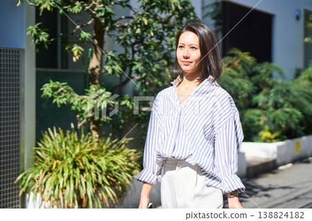 On her way home from shopping, a Japanese woman smiles and enjoys a leisurely stroll on her day off, smartphone in hand. On her way home from shopping, a Japanese woman smiles and enjoys a leisurely stroll on her day off, smartphone in hand. 138824182