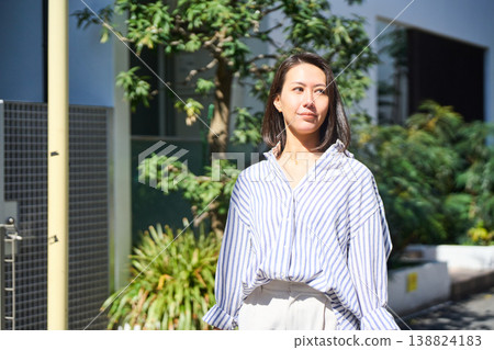 On her way home from shopping, a Japanese woman smiles and enjoys a leisurely stroll on her day off, smartphone in hand. On her way home from shopping, a Japanese woman smiles and enjoys a leisurely stroll on her day off, smartphone in hand. 138824183