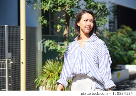 一位日本女性購物回家途中,面帶微笑,悠閒地散步,享受著難得的休息日,手裡拿著智慧型手機。 一位日本女性購物回家途中,面帶微笑,悠閒地散步,享受著難得的休息日,手裡拿著智慧型手機。 138824184