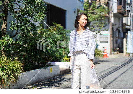On her way home from shopping, a Japanese woman smiles and enjoys a leisurely stroll on her day off, smartphone in hand. On her way home from shopping, a Japanese woman smiles and enjoys a leisurely stroll on her day off, smartphone in hand. 138824186