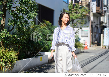 On her way home from shopping, a Japanese woman smiles and enjoys a leisurely stroll on her day off, smartphone in hand. On her way home from shopping, a Japanese woman smiles and enjoys a leisurely stroll on her day off, smartphone in hand. 138824187
