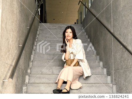 A cool woman in a black knit top and beige pants sits on a modern staircase in Umeda, Osaka. A cool woman in a black knit top and beige pants sits on a modern staircase in Umeda, Osaka. 138824241