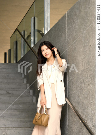 A woman stands on a city staircase, displaying a cool expression, against a modern urban backdrop. 138824411