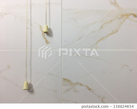 Two pull cords hang from the ceiling in a bathroom with marble wall tiles in a residential space during daytime hours 138824654
