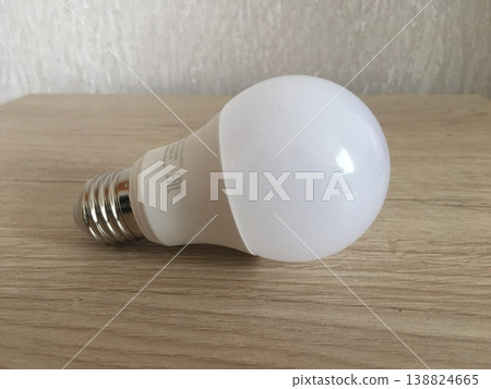 Light bulb resting on wooden surface in a well-lit room showing basic design and structure of common household item Light bulb resting on wooden surface in a well-lit room showing basic design and structure of common household item 138824665
