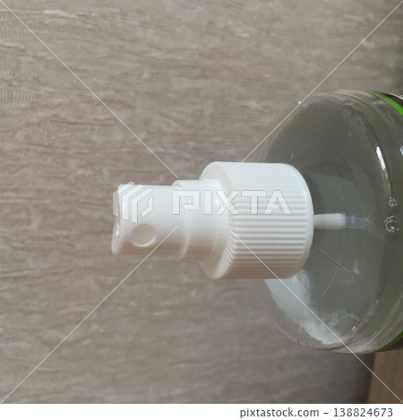 Clear plastic bottle with a white pump dispenser sitting against a textured wall in a well-lit room 138824673