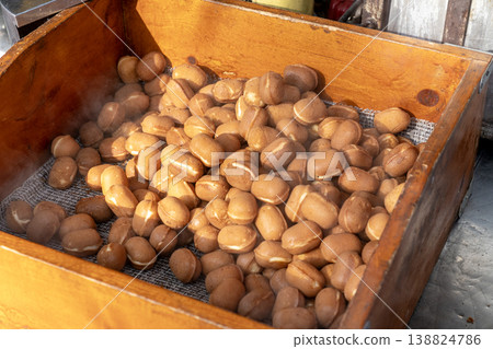 Freshly baked Japanese baby castella sponge cakes inside a rustic wooden crate. Steaming hot golden brown ball shaped snacks from a traditional street food stall. Delicious sweet treats display 138824786