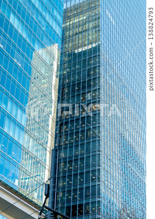 Modern blue glass skyscrapers reflecting urban landscape. Professional office building facades with geometric grid patterns in a corporate business district. Bright daylight and clear window panels. Modern blue glass skyscrapers reflecting urban landscape. Professional office building facades with geometric grid patterns in a corporate business district. Bright daylight and clear window panels. 138824793