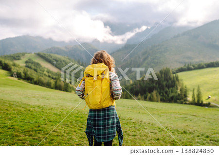 Female tourist with yellow backpack on top of mountain enjoying view of valley. Hiking concept. 138824830