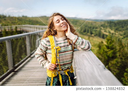 Happy woman with yellow backpack on wooden pedestrian bridge enjoying mountain scenery. Happy woman with yellow backpack on wooden pedestrian bridge enjoying mountain scenery. 138824832