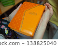 Person Holding Orange Covered Book with Arabic Calligraphy 138825040