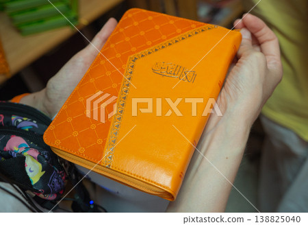 Person Holding Orange Covered Book with Arabic Calligraphy 138825040