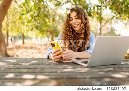 Happy woman with laptop and phone at table in an outdoor near lake. Business, blogging, freelancing. Happy woman with laptop and phone at table in an outdoor near lake. Business, blogging, freelancing. 138825405