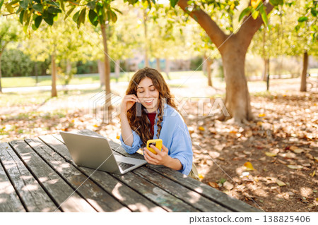 Happy woman with laptop and phone at table in an outdoor near lake. Business, blogging, freelancing. Happy woman with laptop and phone at table in an outdoor near lake. Business, blogging, freelancing. 138825406