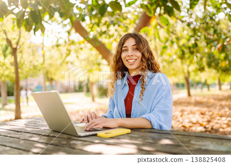Attractive woman working or studying at laptop as sitting in city park. Freelancer working in park. Attractive woman working or studying at laptop as sitting in city park. Freelancer working in park. 138825408