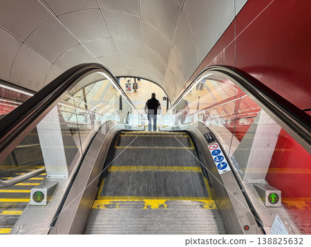 Escalator at railway station leading to platform with passengers and luggage. Escalator at railway station leading to platform with passengers and luggage. 138825632