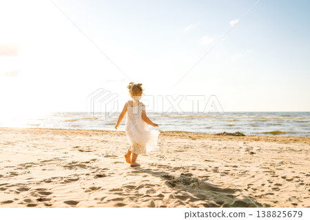 Young girl joyfully plays on the sandy beach during sunset, enjoying a carefree moment by the ocean 138825679