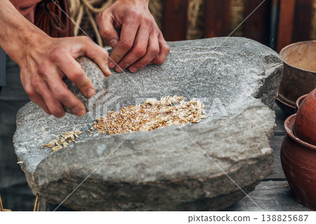 Human hand rotating an ancient stone grinding machine for smashing grains. Handmade manual equipment grind mill 138825687