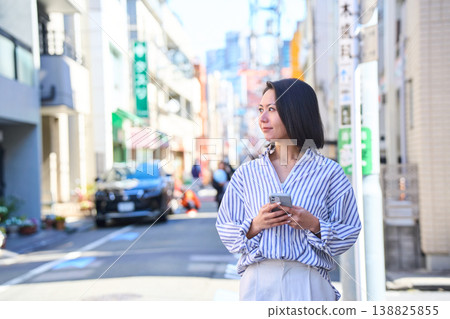 A Japanese woman smiles as she looks at her smartphone while shopping. A stroll through the city on a holiday. 138825855