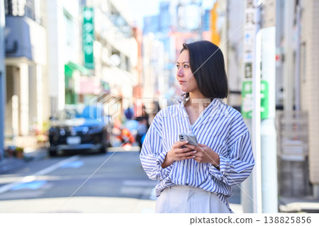 A Japanese woman smiles as she looks at her smartphone while shopping. A stroll through the city on a holiday. 138825856