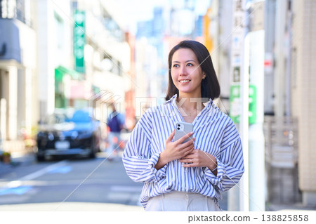A Japanese woman smiles as she looks at her smartphone while shopping. A stroll through the city on a holiday. 138825858