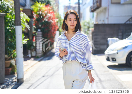 A Japanese woman smiles as she looks at her smartphone while shopping. A stroll through the city on a holiday. 138825866