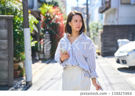A Japanese woman smiles as she looks at her smartphone while shopping. A stroll through the city on a holiday. A Japanese woman smiles as she looks at her smartphone while shopping. A stroll through the city on a holiday. 138825868