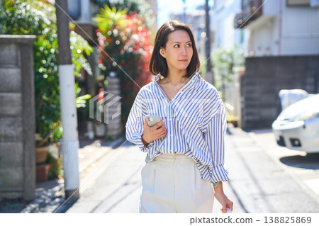 一位日本女子一邊看著手機一邊購物,臉上帶著微笑。這是她在假日裡漫步城市時的照片。 一位日本女子一邊看著手機一邊購物,臉上帶著微笑。這是她在假日裡漫步城市時的照片。 138825869