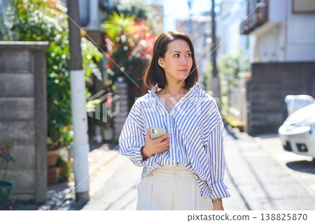 一位日本女子一邊看著手機一邊購物,臉上帶著微笑。這是她在假日裡漫步城市時的照片。 一位日本女子一邊看著手機一邊購物,臉上帶著微笑。這是她在假日裡漫步城市時的照片。 138825870