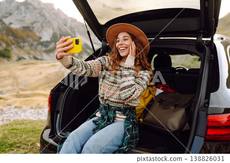 Young traveler woman taking a selfie by her car in the mountains during sunset. Lifestyle, travel Young traveler woman taking a selfie by her car in the mountains during sunset. Lifestyle, travel 138826031
