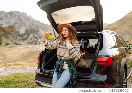 Young traveler woman taking a selfie by her car in the mountains during sunset. Lifestyle, travel 138826032