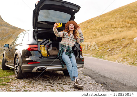 Young traveler woman taking a selfie by her car in the mountains during sunset. Lifestyle, travel 138826034