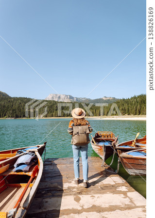 A woman with curly hair poses by the lake on a sunny day, wearing a colorful sweater and hat A woman with curly hair poses by the lake on a sunny day, wearing a colorful sweater and hat 138826169